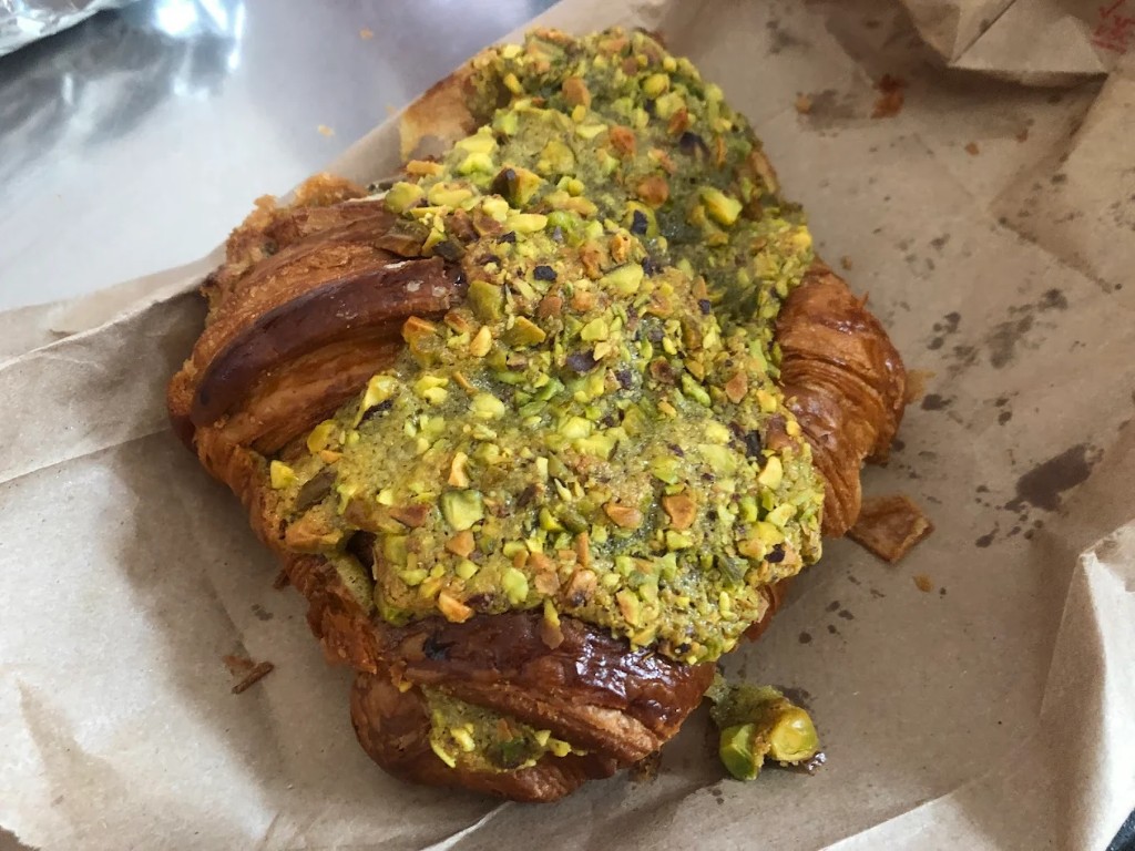 Pistachio croissant with green frangipane and crushed pistachios on a paper bag